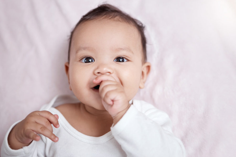 High angle shot of an adorable baby sucking their fingers while laying on a blanket.