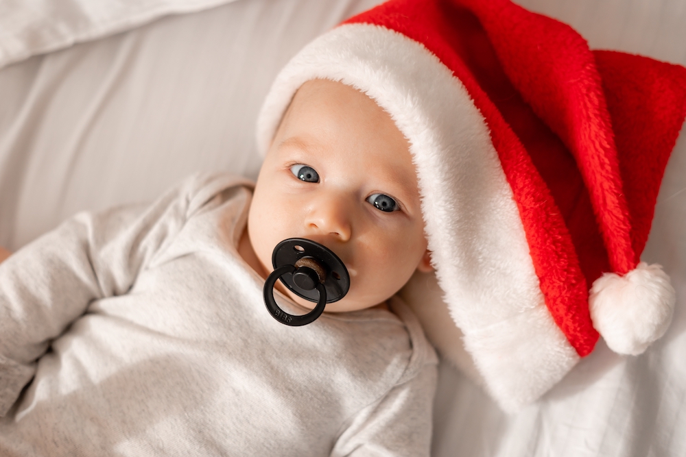 Baby with a pacifier in their mouth and wearing a Santa hat on their head