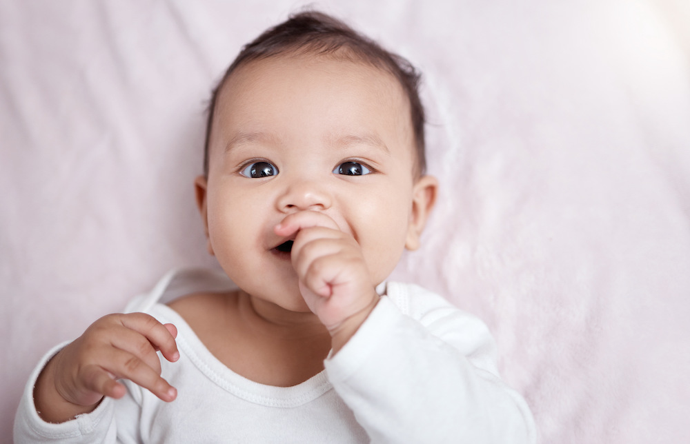 High angle shot of an adorable baby sucking their fingers while laying on a blanket.